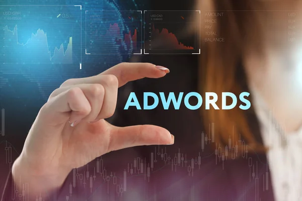 Hand holding the word ADWORDS on a digital screen with financial charts in the background